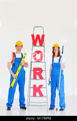 Happy couple in uniform holding tools and ladder with work letters Stock Photo