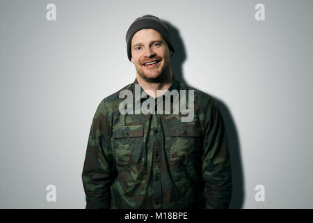 young attractive man wearing camouflage long sleeve shirt and hat on gray background Stock Photo