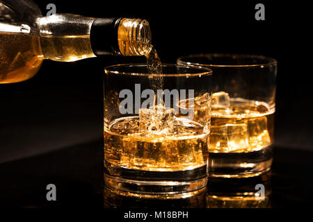pouring whiskey into a glass from bottle with ice cubes on black background Stock Photo