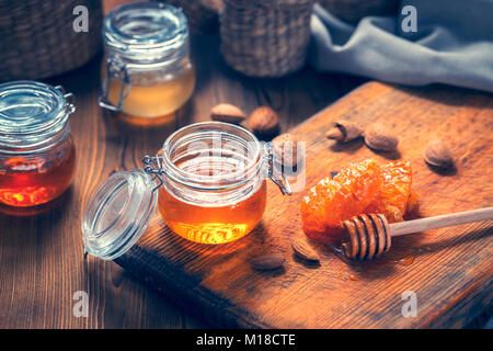Honey in glass jars, nuts almonds and honey dipper on a wooden table. Toned Stock Photo