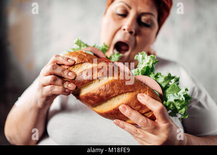 Fat woman eats sandwich, overweight and bulimic. Unhealthy lifestyle. Obesity Stock Photo