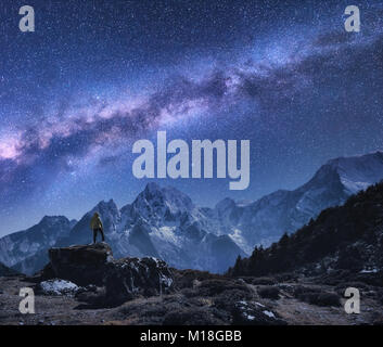 Space with Milky Way and mountains. Standing man on the stone, mountains and starry sky at night in Nepal. Rocks with snowy peaks against sky with sta Stock Photo