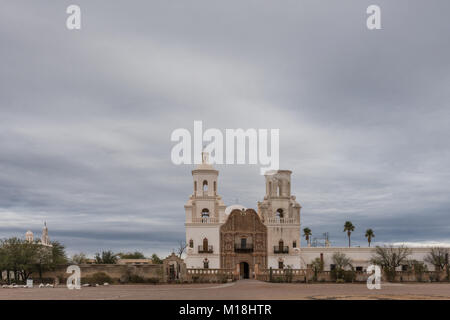 Tucson, Arizona, USA - January 9, 2018: Wide view on White and brown front facade of Historic San Xavier Del Bac Mission under heavy gray, white cloud Stock Photo