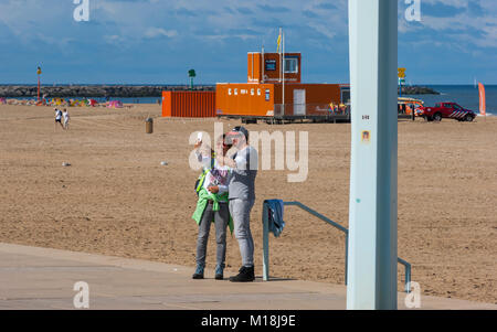 Couple taking a selfie on the beach esplanade in Scheveningen. A lifeguard station can be seen in the background. The Hague (Den Haag), Netherlands Stock Photo