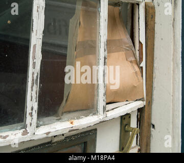 Close up of a door with a broken window pane replaced with a piece of cardboard. Stock Photo