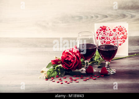 Two glasses of red wine, rose with decoration by red hearts on wooden table. Valentine's day celebration concept. Copy space. Stock Photo