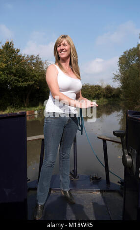 Woman using the tiller to steer a narrowboat along a canal in the UK Stock Photo