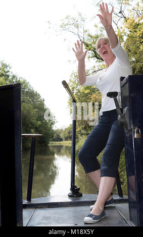 Woman using the tiller to steer a narrowboat along a canal in the UK Stock Photo