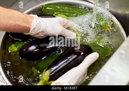 Washing two black eggplants in metal bowl with bubble water. Stock Photo