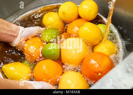 Plenty of citrus fruits in a metal bowl full of water under tap water. Stock Photo