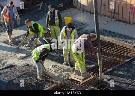 Workmen  in high visibility flourescent jackets on building, pouring concrete into foundations Stock Photo