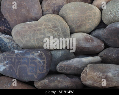 Buddhist prayer stones: on the river rounded boulders are painted ancient Tibetan mantras in Sanskrit. Stock Photo