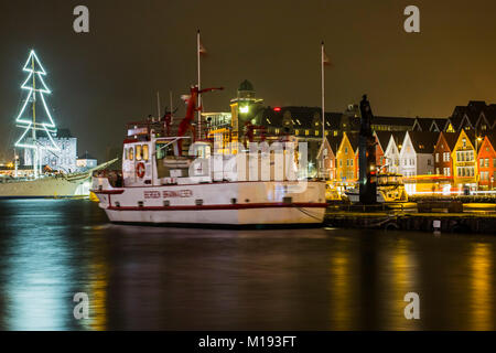 City Fire Department ship & statue of WWII naval hero Leif Andreas Larsen on historic Bryggen waterfront at night. Bergen, Hordaland, Norway. Stock Photo