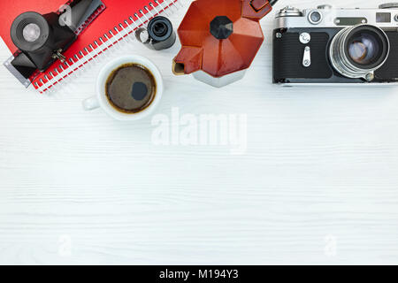 retro camera, roll films, lens, notebook and grunge red coffee pot on white wooden background Stock Photo