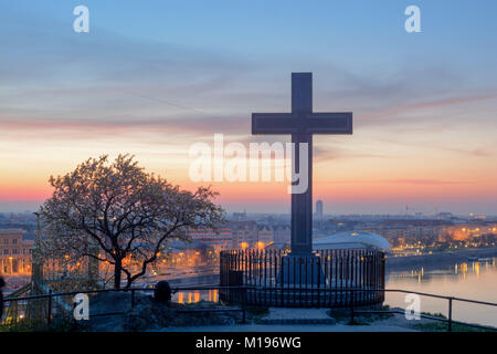 Blooming tree and Stone cross located on Gellért Hill above Cave Church. Night view against Budapest city Stock Photo