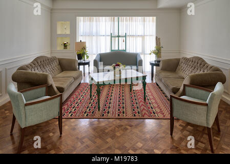 Interior shot of luxury modern living room with three couches, two armchairs, and vintage wooden table on background of big window with white curtains Stock Photo