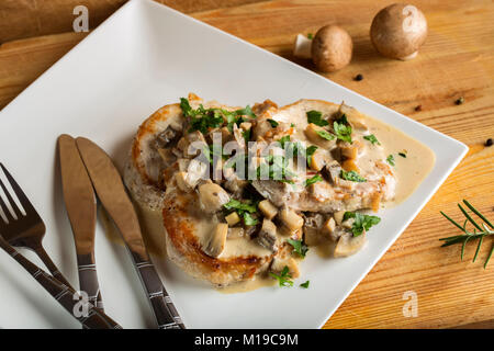 Pork sirloin with white sauce made from sour cream and mushrooms with two knifes and forks Stock Photo