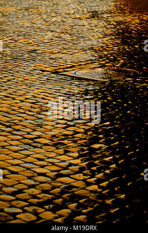 Wet cobbled street at night lit by yellow lights Stock Photo