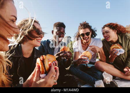 Young people having summer picnic and eating together sitting on mountain top. Happy friends on mountain top having a picnic on a summer day. Stock Photo
