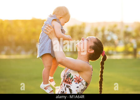 Close-up Of A Smiling Mother Carrying Her Baby Daughter In Garden Stock Photo