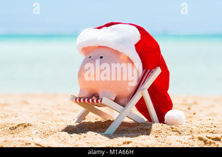 A Pink Piggy Bank With Santa Hat Kept On The Deck Chair At Beach Stock Photo