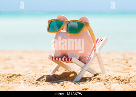 Pink Piggy Bank Wearing Wooden Sunglasses Kept On The Deck Chair At Beach Stock Photo