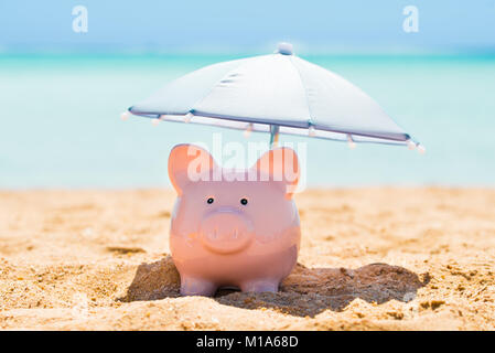 Pink Piggy Bank Under The Small Parasol During Summer At Beach Stock Photo