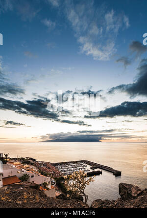 View westwards at sunset over the harbour of Los Gigantes, Tenerife, Canary Islands towards the island of La Gomera  with spectacular sky and calm sea Stock Photo