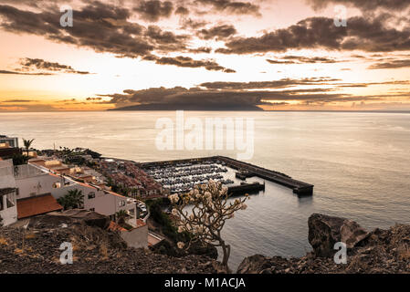 View westwards at sunset over the harbour of Los Gigantes, Tenerife, Canary Islands towards the island of La Gomera  with spectacular sky and calm sea Stock Photo