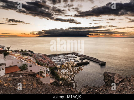 View westwards at sunset over the harbour of Los Gigantes, Tenerife, Canary Islands towards the island of La Gomera  with spectacular sky and calm sea Stock Photo