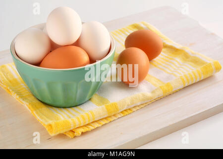 Brown and white eggs in green bowl on yellow checked tea towel in horizontal format and shot in natural light Stock Photo