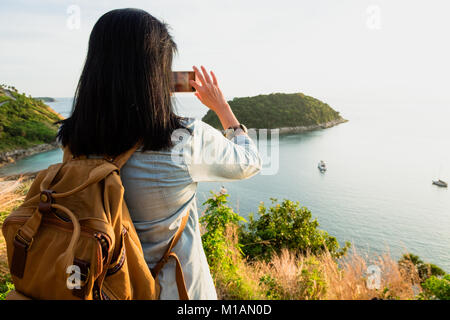 Asia Young traveler woman backpacker use mobile phone take a photo of beautiful of sunset nature at top of mountain sea view,Freedom wanderlust concep Stock Photo