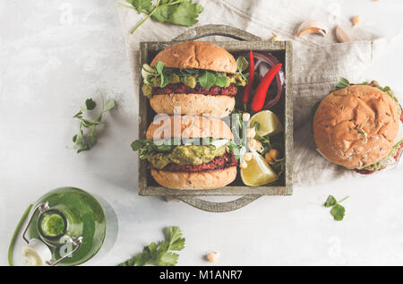 Vegan beet chickpea burgers with vegetables, guacamole and rye buns in wooden box. Healthy vegan food concept. Stock Photo