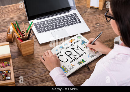 Close-up Of A Businesswoman Drawing CRM Plan On Notebook At Workplace Stock Photo