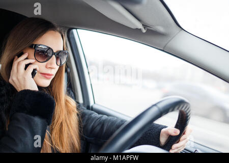 Young woman drive a car in winter. Smiling european woman using smartphone inside a car Stock Photo