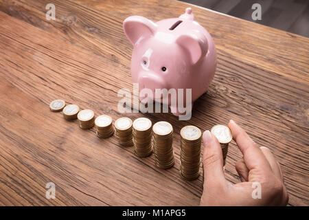 Close-up Of A Woman Placing A Coin Over The Increasing Stack On Wooden Desk Stock Photo
