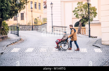 Senior father in wheelchair and young son on a walk. Stock Photo