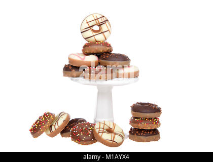 Many small donuts coated in candy and decorated with sprinkles stacked on a small pedestal with extras on the table, isolated on white. Stock Photo