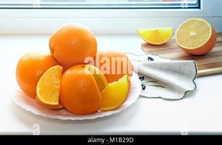 On the windowsill a plate of large oranges, some of them cut into slices. Stock Photo