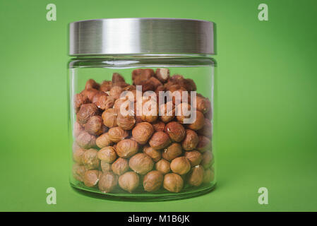 Hazelnuts in glass jar, isolated on green background Stock Photo