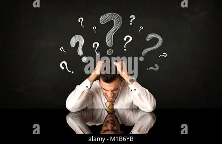 Depressed businessman sitting under question marks Stock Photo