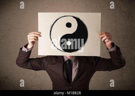 Businessman holding a paper with a yin-yang symbol on it in front of his head Stock Photo