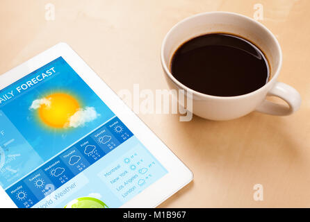 Workplace with tablet pc showing weather forecast and a cup of coffee on a wooden work table close-up Stock Photo