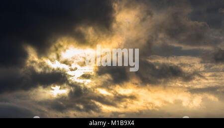Orange rain clouds in the sky with dark blue clouds and sunbeams during sunset. Stock Photo