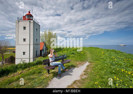 The Netherlands, Oosterdijk, Woman on bench near former lighthouse at lake called IJsselmeer. Stock Photo