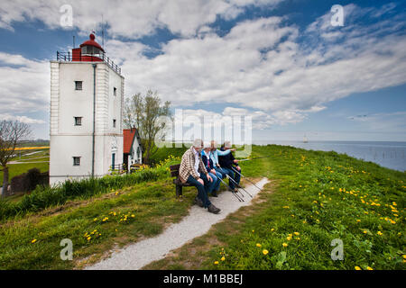 The Netherlands, Oosterdijk, Hikers on bench near former lighthouse at lake called IJsselmeer. Stock Photo