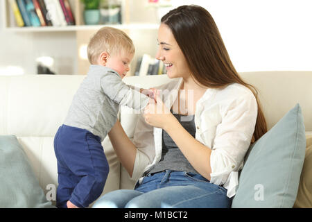 Proud mother helping to her baby to stand on a couch in the living room at home Stock Photo