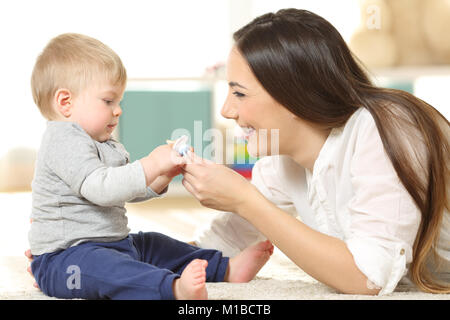 Side view portrait of a proud mother giving a pacifier to her baby on the floor at home Stock Photo