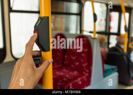 A male passenger is pressing red STOP button with his index finger on London Bus, UK Stock Photo