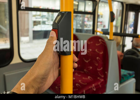 A male passenger is pressing red STOP button with his thumb on London Bus, UK Stock Photo